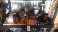 Full view of multiple kitchen items on a shelf including teapots, pots, wooden knife handles, decorative pieces.