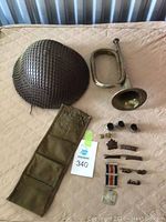 Overhead view of helmet, bugle, canvas pouch, tin cups and insignia laid out on bedspread