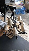 Full view of large black metal chandelier with fabric lampshades placed on the floor, showing its ornate scrollwork design and overall condition.