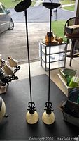 Full view of both hanging pendant lamps showing black metal rods and frosted glass shades, placed on floor indoors.