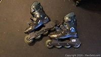 Pair of used black inline roller blades with adjustment straps laid on dark carpet