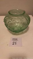 Green flower-patterned embossed glass vase with round shape and translucent green tint.