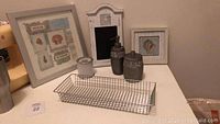 Nine ocean themed bathroom items arranged including framed pictures, dispensers, wire towel tray and new shower wand box