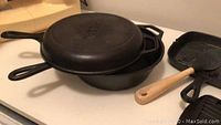 Photo showing three cast iron skillets stacked, including one acting as a lid, a wooden-handled brush, and a ridged cast iron grill pan.