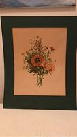 Photo of vintage art print showing a flower bouquet with green matting, unframed, displayed against a wall.