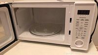 Open door image showing clean interior with glass turntable and control panel with numeric keypad and dial