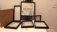 Six black-bordered picture frames arranged on a flat surface. One has ornamental iron scrollwork and 'HOME' text insert.