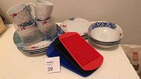 Full view of ceramic mugs, plates, bowls with floral patterns and three silicone mini ice cube makers in different colors.
