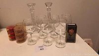 Wide view photo showing six stemmed wine glasses, two tall clear candlesticks, three cylindrical containers with floating candles, and a small black box with a pumpkin wine cork.