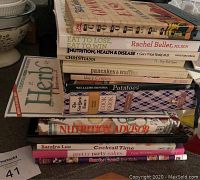 Photo showing a stacked assortment of vintage cookbooks including Betty Crocker editions and books on nutrition, pancakes, potatoes, cocktails, and party cakes.