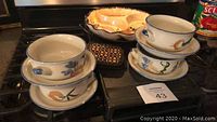Photo of four ceramic Chinese soup bowls stacked on matching plates, six bamboo coasters, ceramic serving dish with metal stand visible in background.