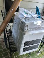 Side view of large white window air conditioner unit sitting on metal rack outdoors.