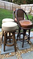 Photo showing 6 vintage stools outdoors with gravel ground. Four high-back stools with wood and cane backs, two padded fabric stools in front.