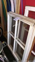 Two vintage wooden framed four pane windows stacked leaning against a red wall