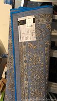 Rolled and tagged folded edge showing label with Kashan Collection branding, details of size, pile height, fibers composition, color blue