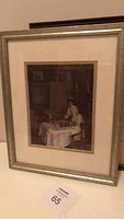 Framed art photo showing woman seated at table inside silver-painted wood frame with cream mat