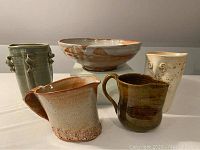 Front view of the five artisan pottery pieces, showing a large bowl, two pitchers and two vases in earthy tones and varied shapes.