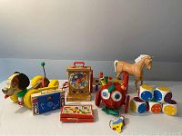 Full view of vintage toys assortment including articulated horse, Playskool pounding bench, Fisher Price Tick Tock clock, pull dog, Wacky Apple pull toy, foam dice, puzzle, and spinning top.