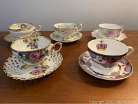 Five cups and saucers displayed together showing the variety of floral designs and gold trim