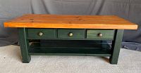 Front view of pine wood coffee table showing natural wood top, forest green base, three drawers with metal knobs, and bottom shelf.