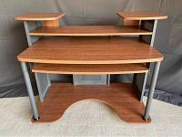 Front view of multi-level computer desk showing wood laminate surfaces, retractable keyboard tray, metal tubular legs, and two small elevated side platforms on the top shelf.