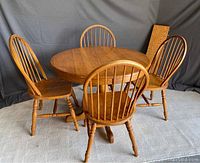 Round solid oak dining table with four matching spindle back chairs, set against a gray backdrop.