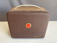 Front view of closed brown textured projector casing with cream handle, Kodak round red logo, and 'OneSix' gold text emblem.