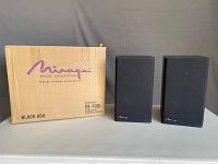 Pair of Mirage M190i speakers standing next to their original box marked Mirage Loudspeakers, model M-190i in Black Ash finish.
