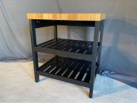 Front angle view of the kitchen island showing butcher block top and two slatted shelves