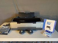 Printer with accessories laid out on table including bagged cables, two disc spools and User’s Guide