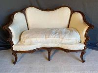 Full front view of vintage settee showing cream upholstery and large seat cushion with slight wear.