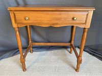 Front view of a medium brown wooden occasional table with turned legs, single drawer with brass knobs, and stretcher bars for support.