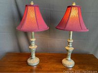 Pair of decorative lamps on a wooden surface, showing the overall style and condition including burgundy fabric shades and silver finish bases.