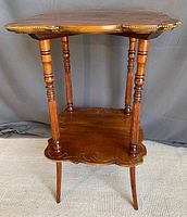 Front view of the vintage occasional table showing the shaped top with brass stud edging and the lower shelf with engraved scalloped design and four turned legs.
