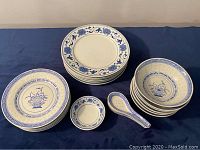 Photo showing stacked luncheon side plates, smaller side plates, bowls, spoons, and sauce bowls arranged on a blue cloth.
