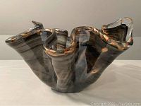 Side angle showing the wavy ruffled edge and brown fleck coloration on grey glass surface.