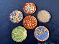 Top view of six decorative Asian ceramic plates arranged on dark fabric background showing vibrant floral and geometric patterns.