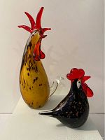 Both handblown glass rooster and hen sculptures shown together on white surface against plain background.