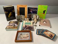 Overview photo showing entire lot including books, notebook, photo frames, coasters, figurines, pin, and note cards arranged on a table.