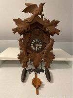 Front view of entire wooden cuckoo clock including weights and pendulum.