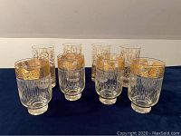 Eight vintage clear glasses with two different styles and gold tone decorative accents arranged in two rows