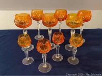 All ten orange pinwheel crystal goblets displayed on a dark cloth, six large and four small.