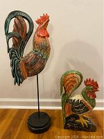 Large and smaller carved wooden roosters, showing scale and details of the figures on stand and base