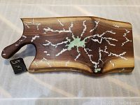 Top view of the walnut cutting board showing white and green resin inlay details, natural edge, and handle.
