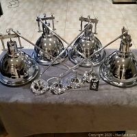 Front view of all four polished chrome ceiling lights laid out on a grey cloth surface, showing the dome shades, arms, and mounting hardware.