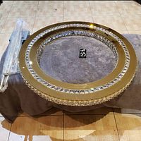 Photo of the circular crystal chandelier laid flat showing the gold metal frame embedded with clear faceted crystals and packaged mounting rods next to it.