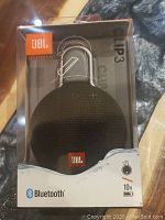 Front view of boxed JBL Clip3 speaker showing the speaker through clear window, JBL logo, Bluetooth logo, and 10 hour battery icon.