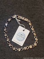 Silver-tone Swarovski bracelet with clear crystals and attached tag placed on dark fabric background.