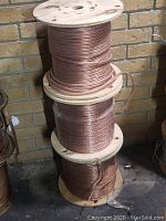 Three wooden reels stacked vertically, each wound with clear-insulated copper speaker wire.