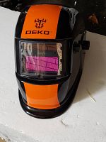 Front view of the Deko welding helmet showing orange and black color scheme and protective viewing window with purple tint.